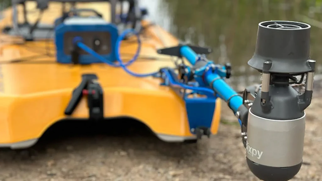 Bixpy K-1 motor mounted on the side of a yellow fishing kayak at the shoreline