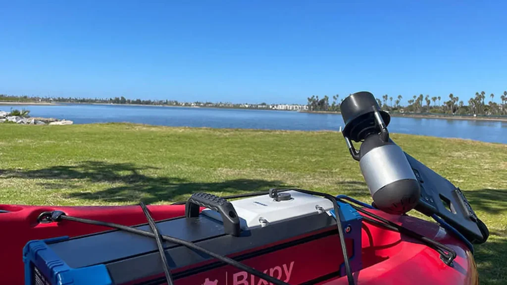 Bixpy K-1 motor and battery pack mounted on a red Mirage Sport kayak by the shoreline