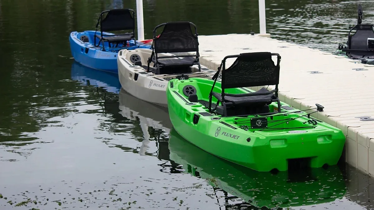 FluxJet Kayak Review: Weed-Ready Electric Jet Power Without an Exposed Prop 3 Three FluxJet electric fishing kayaks in blue, white, and green docked at a marina